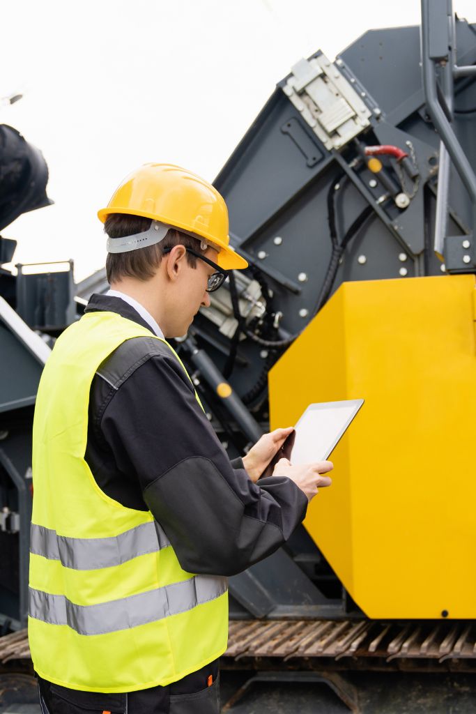 A construction supervisor using a tablet in front of heavy machinery, demonstrating the integration of IT solutions on-site.