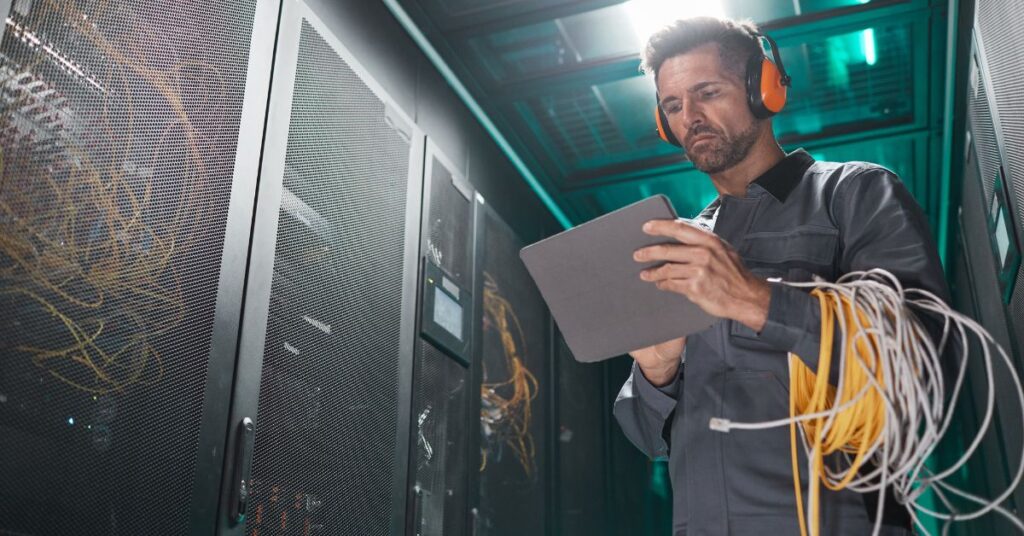 An IT GOAT technician working in a data center, using a tablet and managing ethernet cables to ensure optimal network operations.