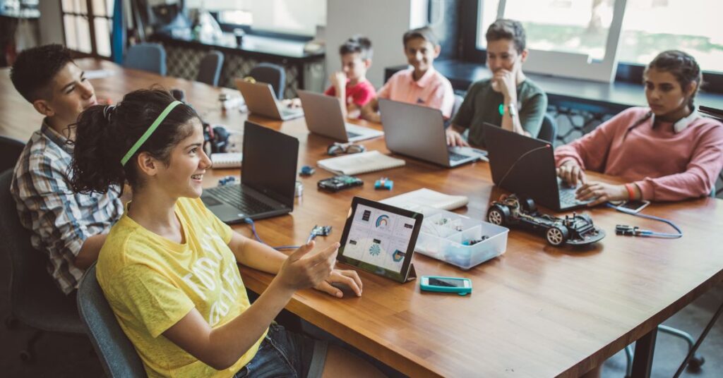 Group of students using laptops and tablets in a modern classroom, engaged in hands-on learning activities with educational technology, facilitated by IT GOAT’s innovative solutions.